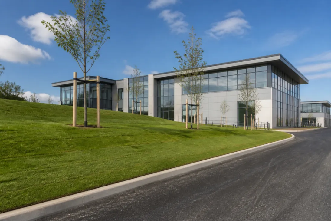 Freshly turfed grass verges and mounds beside an access road on a modern business park with a glass office