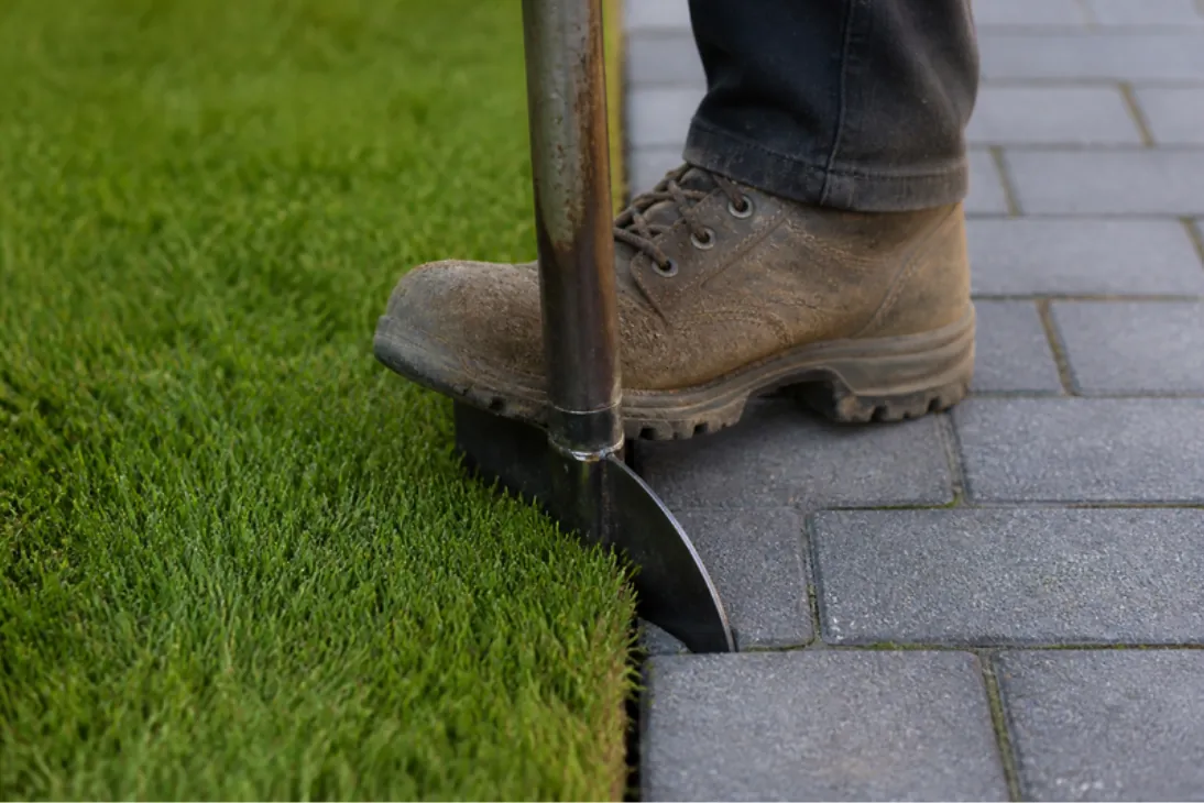 Half-moon edging iron cutting a clean new turf edge against grey block paving