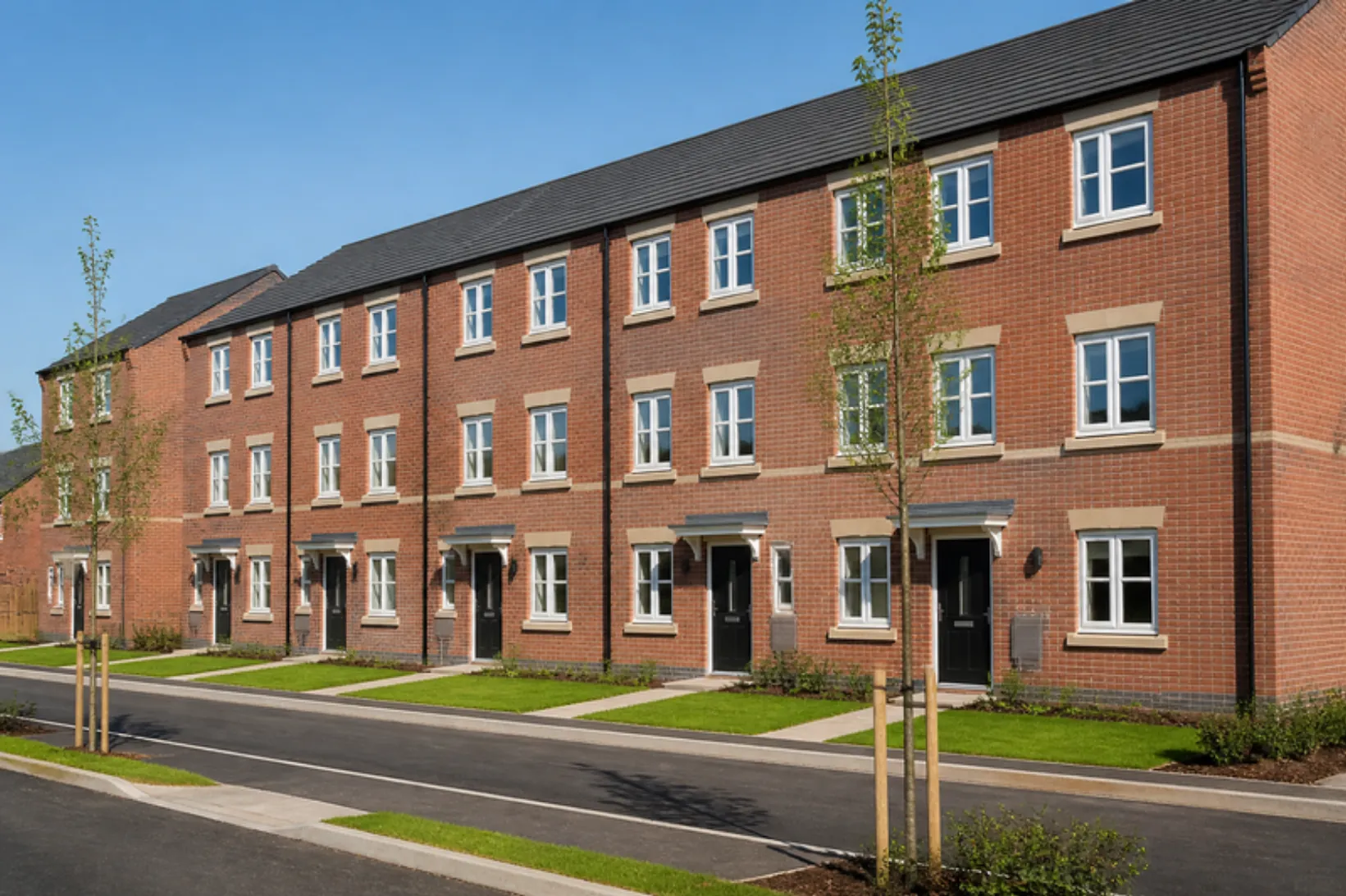 Three-storey red-brick new-build townhouses in Greater Manchester with small new front lawns and staked street trees